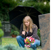 A woman holding an umbrella and leaning down to place flowers at a grave